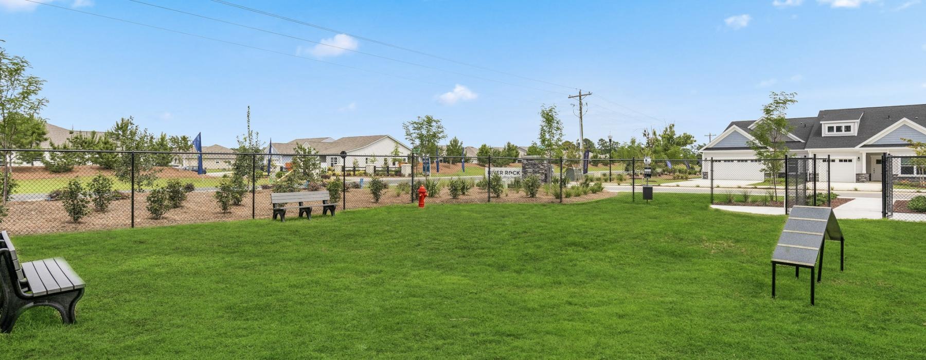 The dog park at our 55 and older rental homes in Dallas, NC, featuring benches, a lawn, and view of the community.